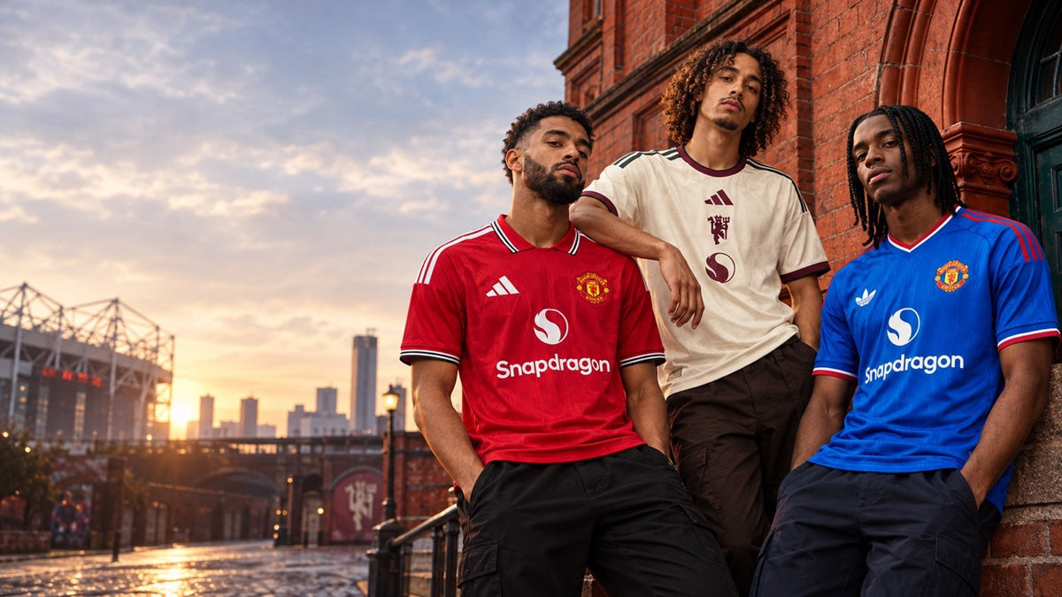 Trois modèles portant les maillots Manchester United 2026/27 : domicile rouge, extérieur bleu et third beige, devant Old Trafford à Manchester.